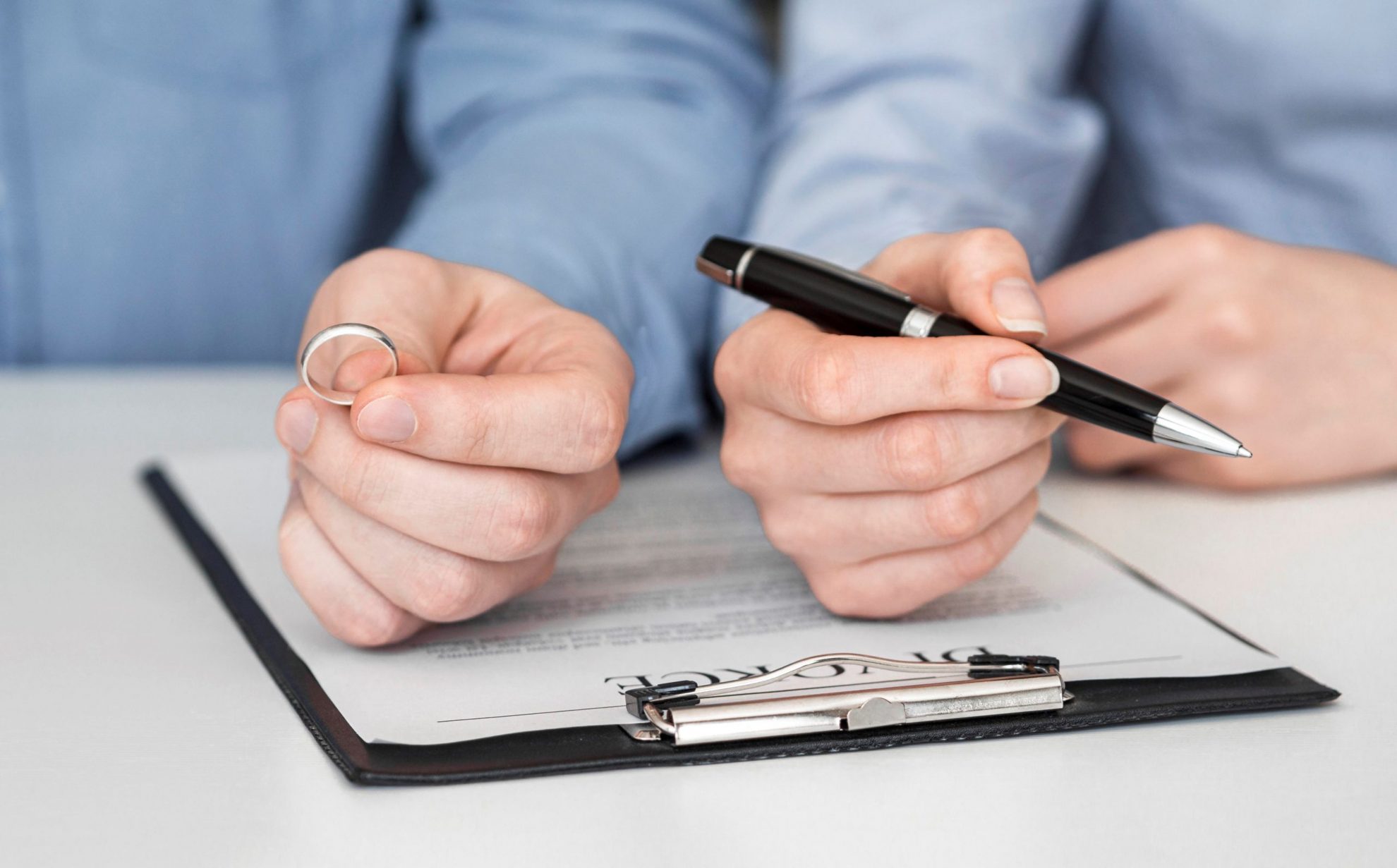 divorce-lawyer-FP Closeup of couple holding wedding ring and pen illustrates blog "How To Choose the Right Divorce Attorney"