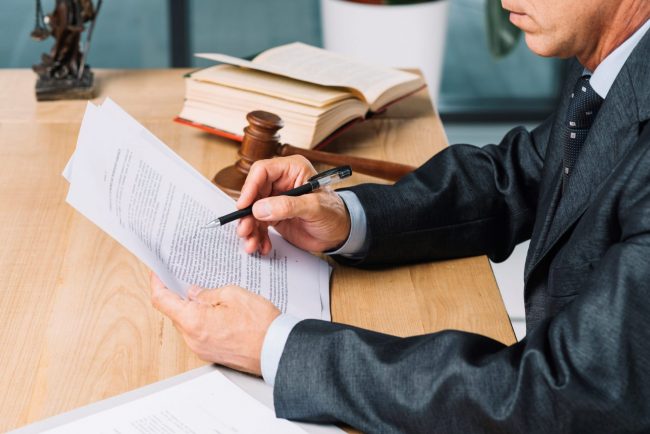 lawyer-FP Lawyer at his desk reading paper with pen in hand illustrates blog "4 Reasons To Hire an Immigration Lawyer"