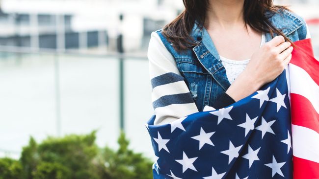 asylum-FP Woman with American flag draped across her shoulders illustrates blog "How Does Asylum Work in the United States?"
