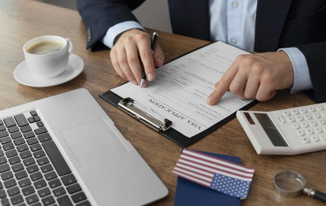 immigration-law-fp Man sitting at desk with laptop and American flag in front of him illustrates blog "What Is Immigration Law?"